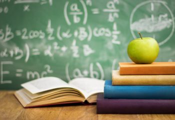School books with apple on desk over green  school board background